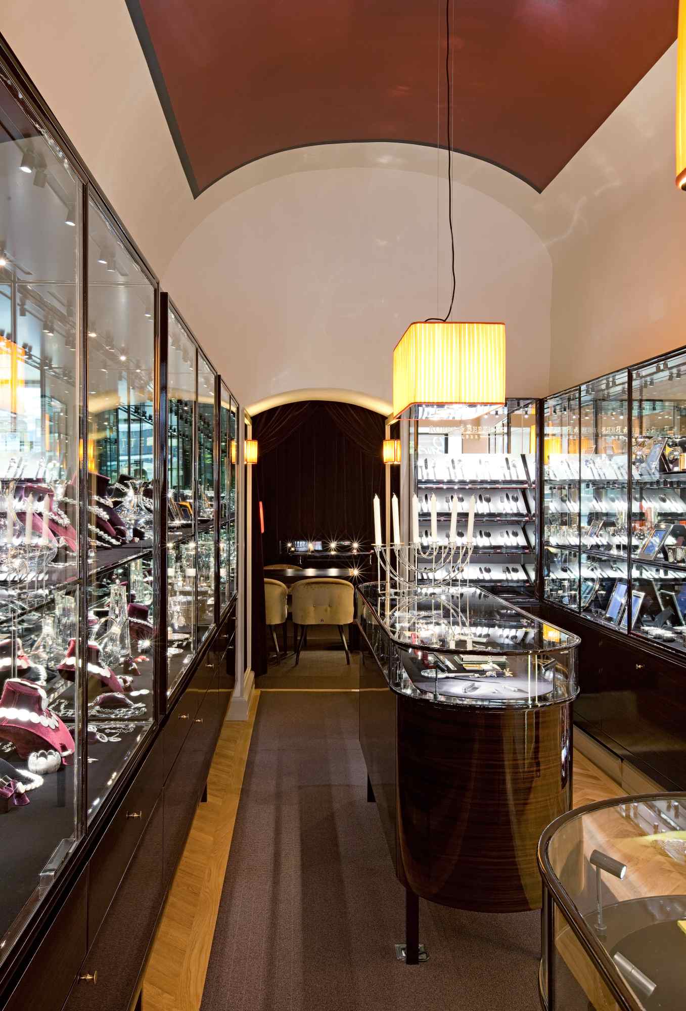 Schmaler Gang mit beidseitig beleuchteten Glasvitrinen unter Tonnengewölbe.