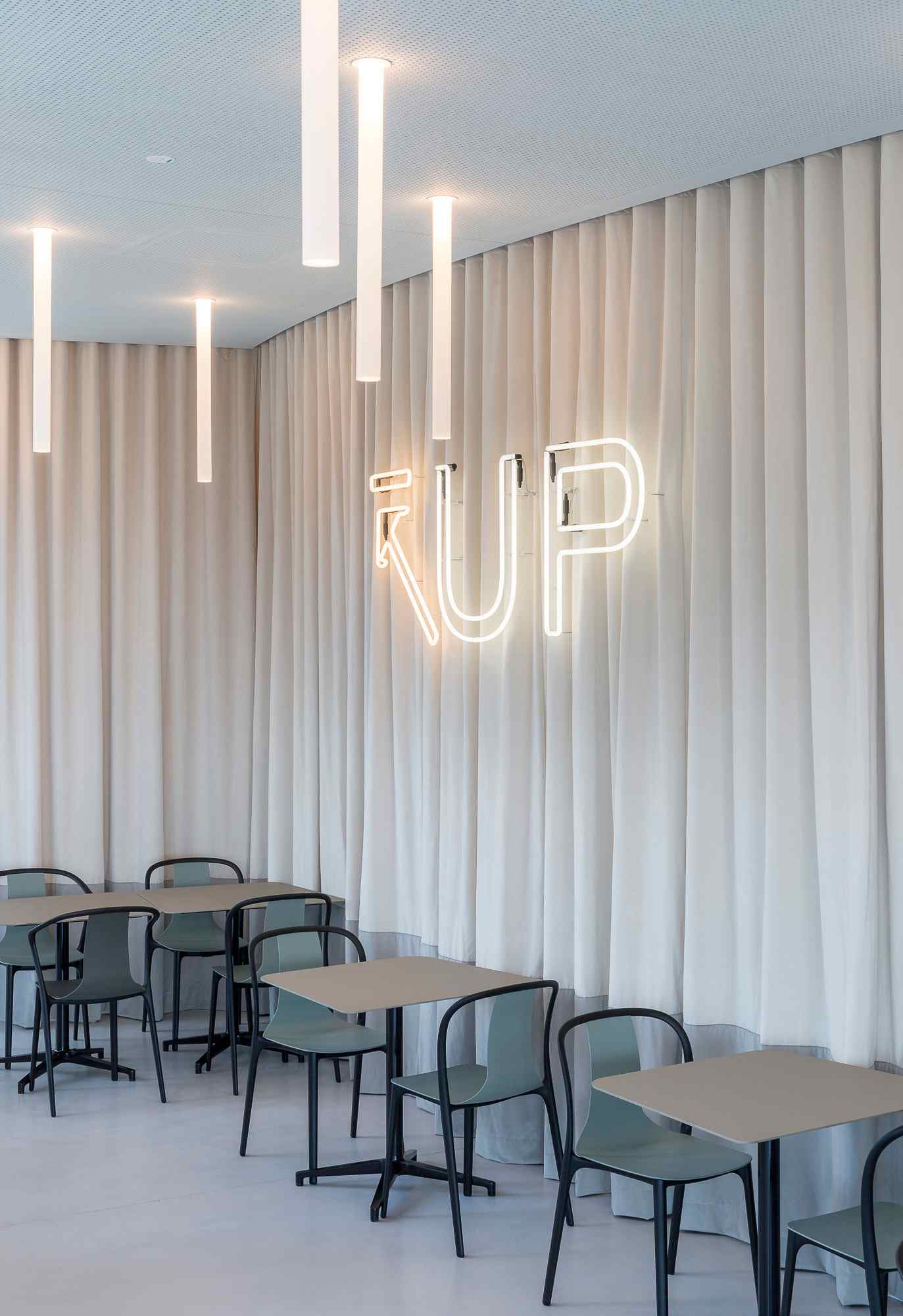 Sitzbereich mit weißen Vorhängen und „UP“-Neonlicht