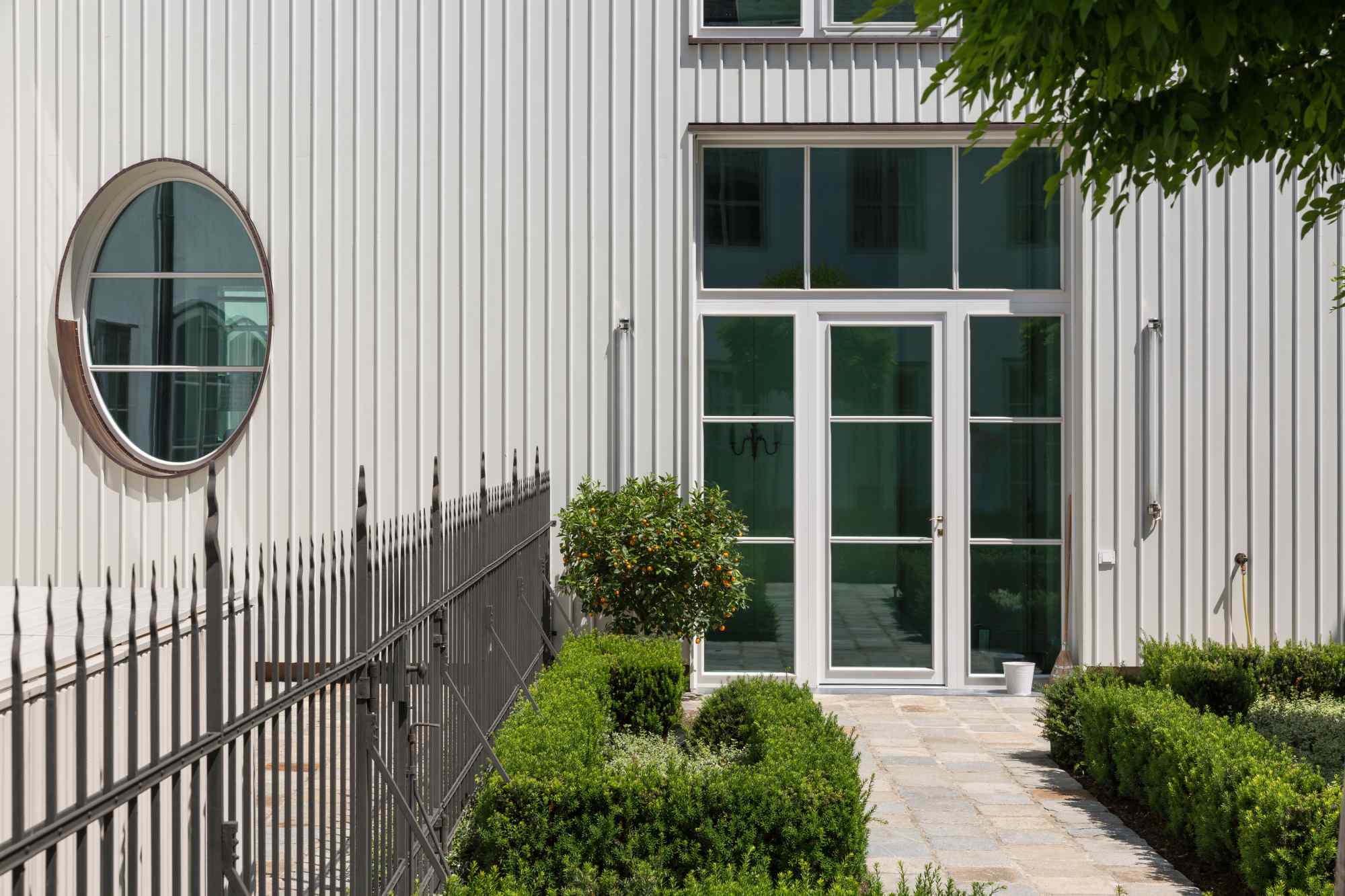 Rundes Fenster, weiße Fassade und kleiner Baum daneben