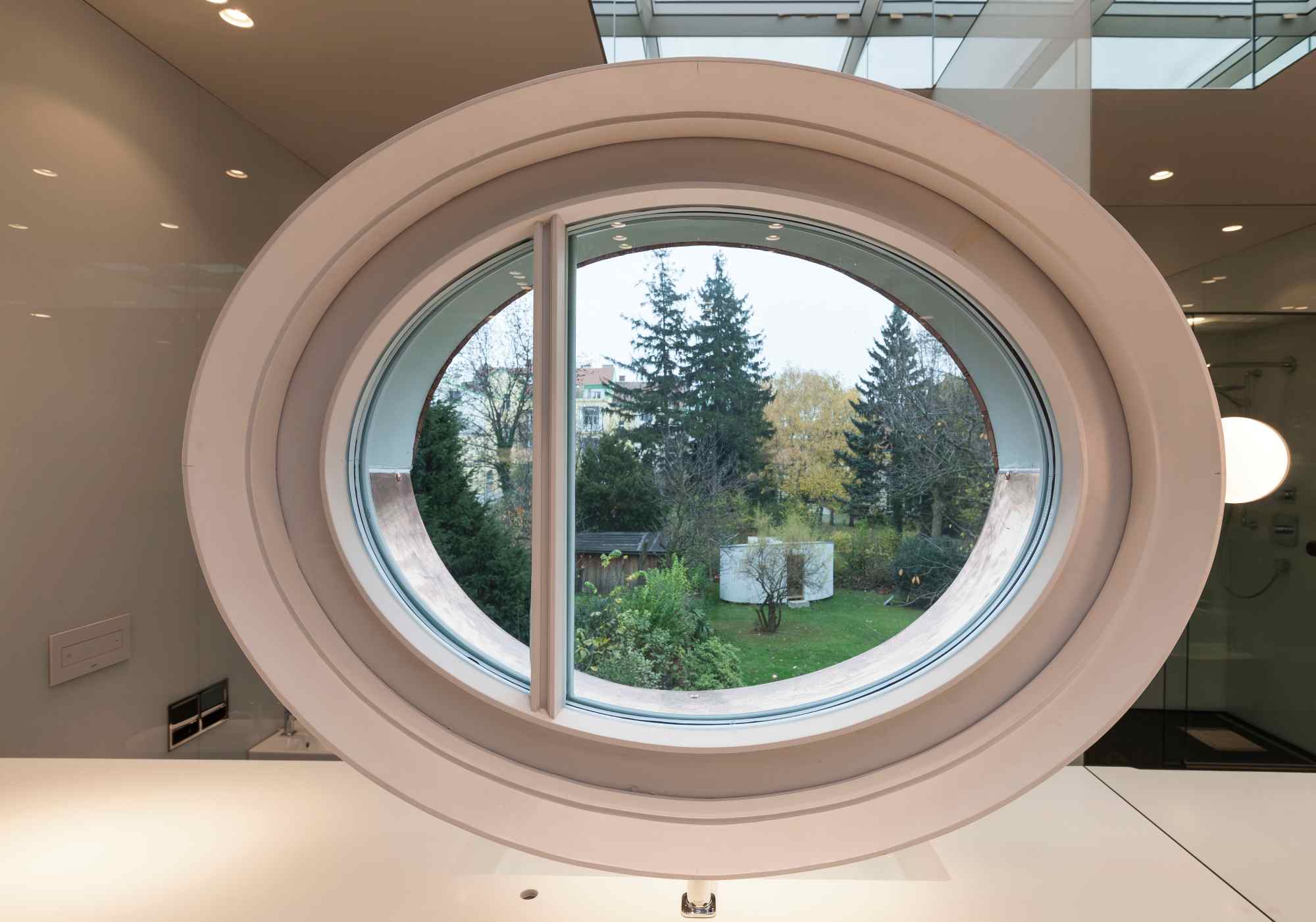 Ovales Fenster mit Blick ins Grüne, innen liegende Holzbank