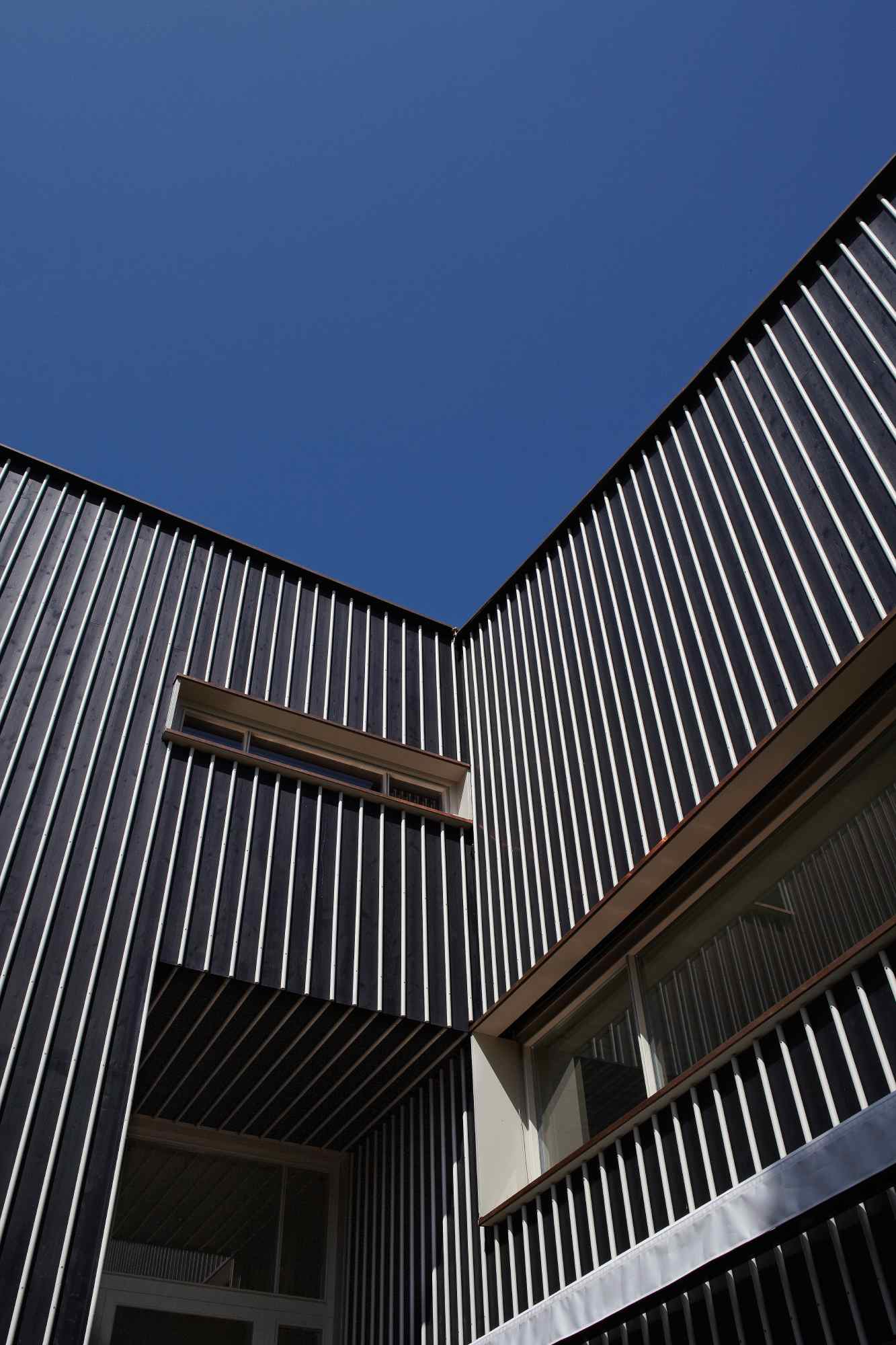 Blick nach oben zwischen zwei Fassadenflächen mit senkrechter Holzlattung