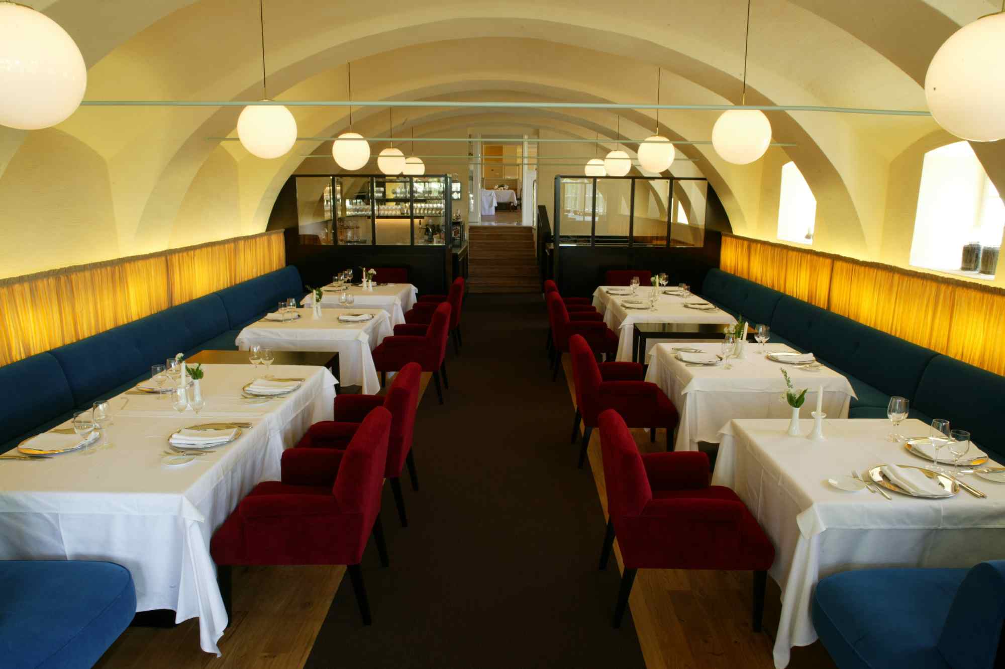 Innenraum mit weißen Tischdecken, roten Sesseln und Tonnengewölbe in edler Restaurantatmosphäre