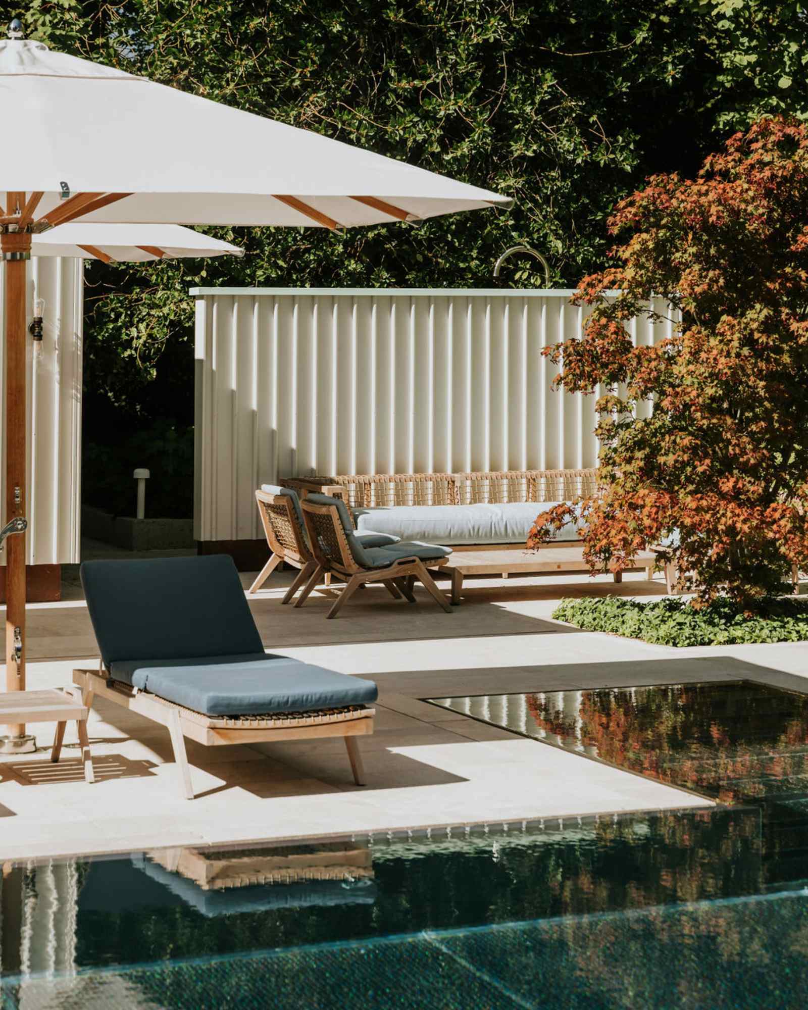 Sonnige Terrasse mit Liegen und weißem Sonnenschirm am Pool