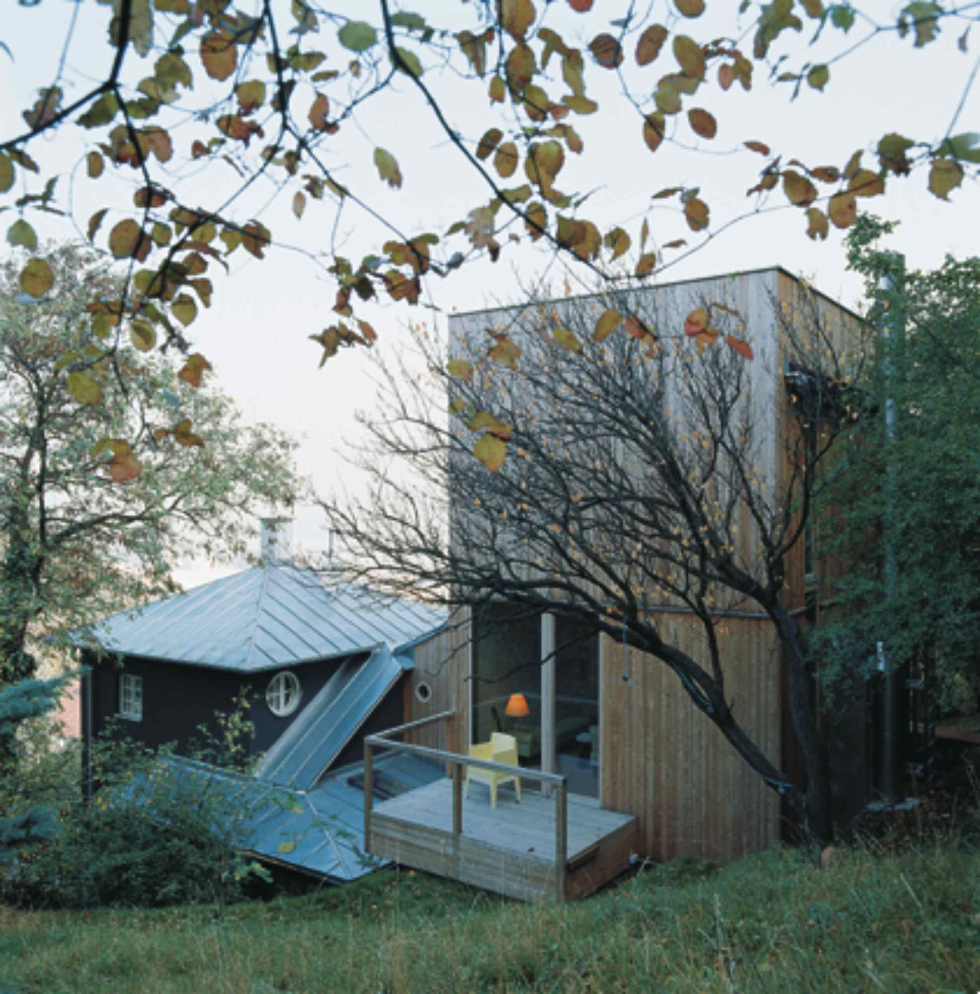 Kombination aus Holz- und Blechfassade mit versetzten Baukörpern und Bäumen im Vordergrund.