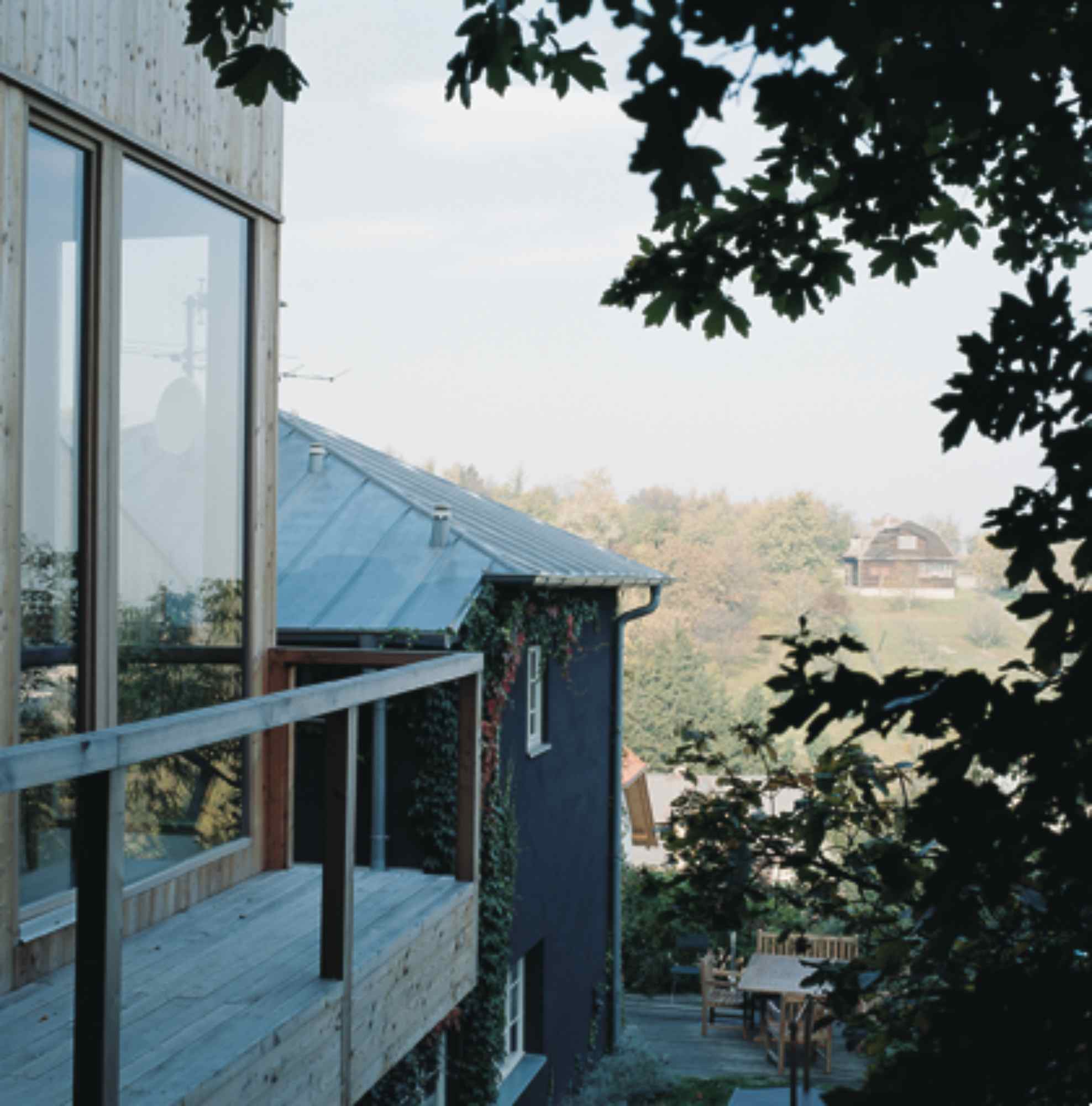Blick vom Balkon mit Holzgeländer ins Tal, eingerahmt von Baumkronen.