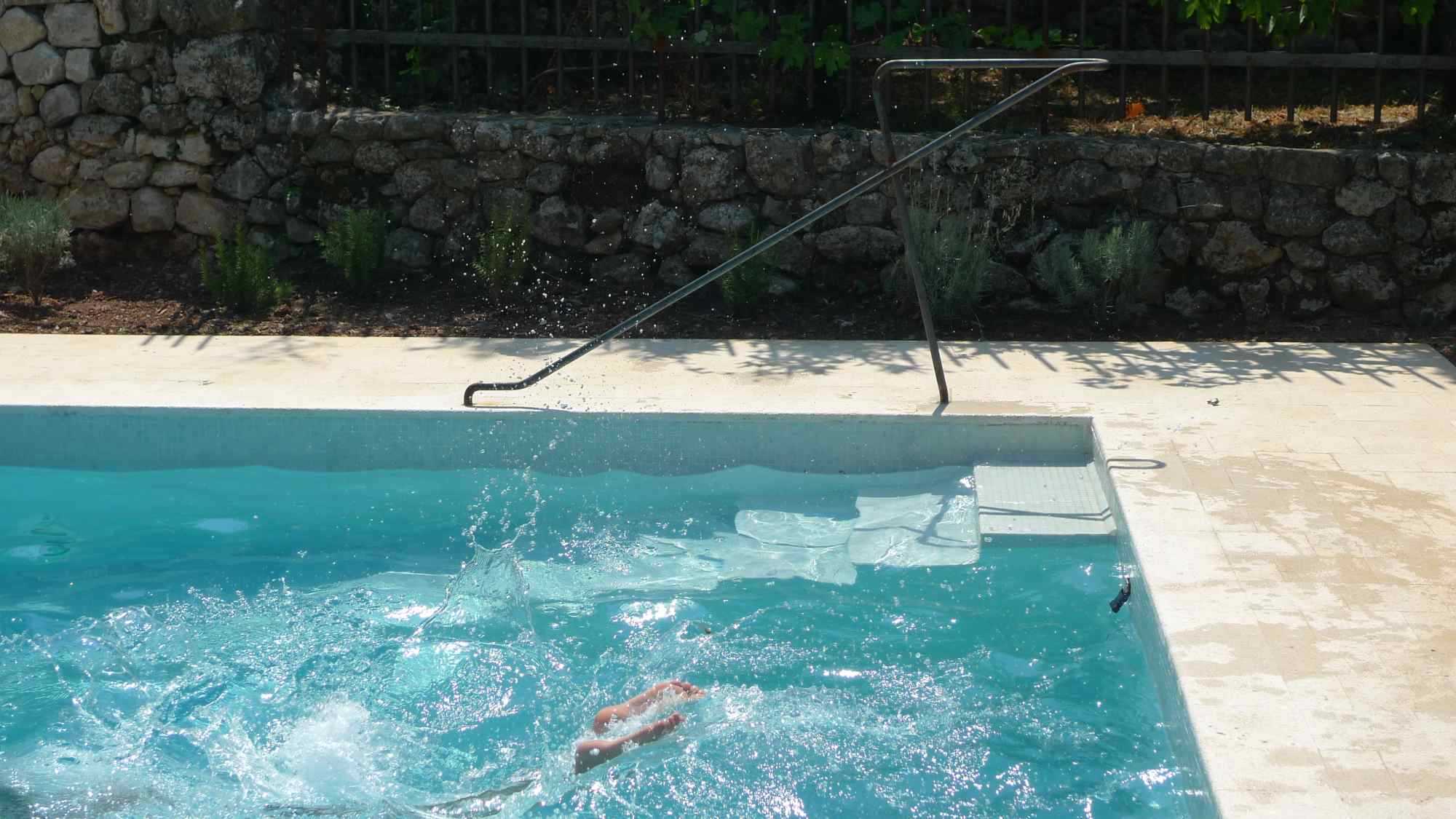Schwimmbecken mit sprudelndem Wasser im Vordergrund, Steinmauer und Natur im Hintergrund.