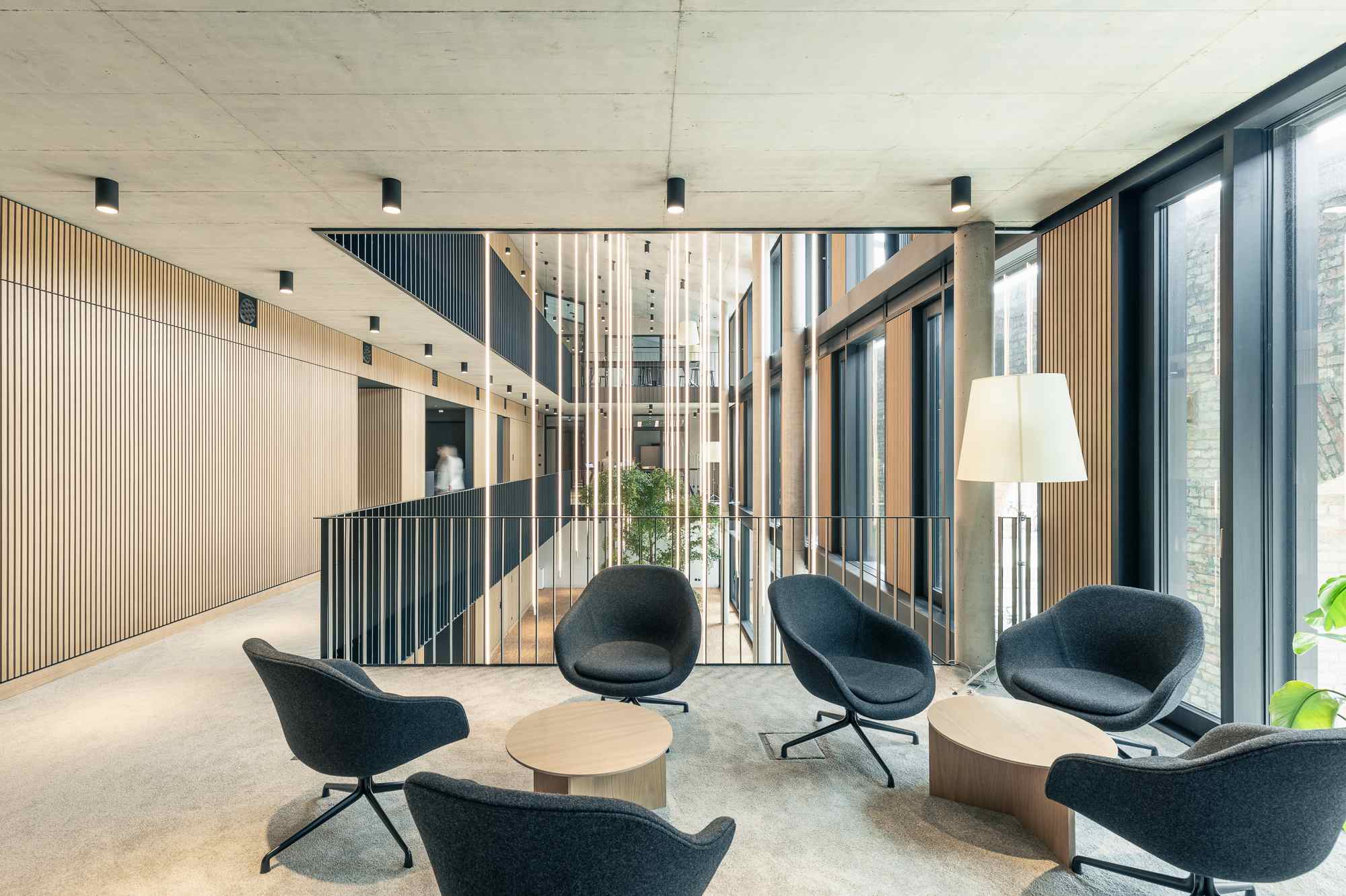 Lounge-Ecke mit modernen Sesseln und Beistelltischen vor großflächiger Fensterfront.