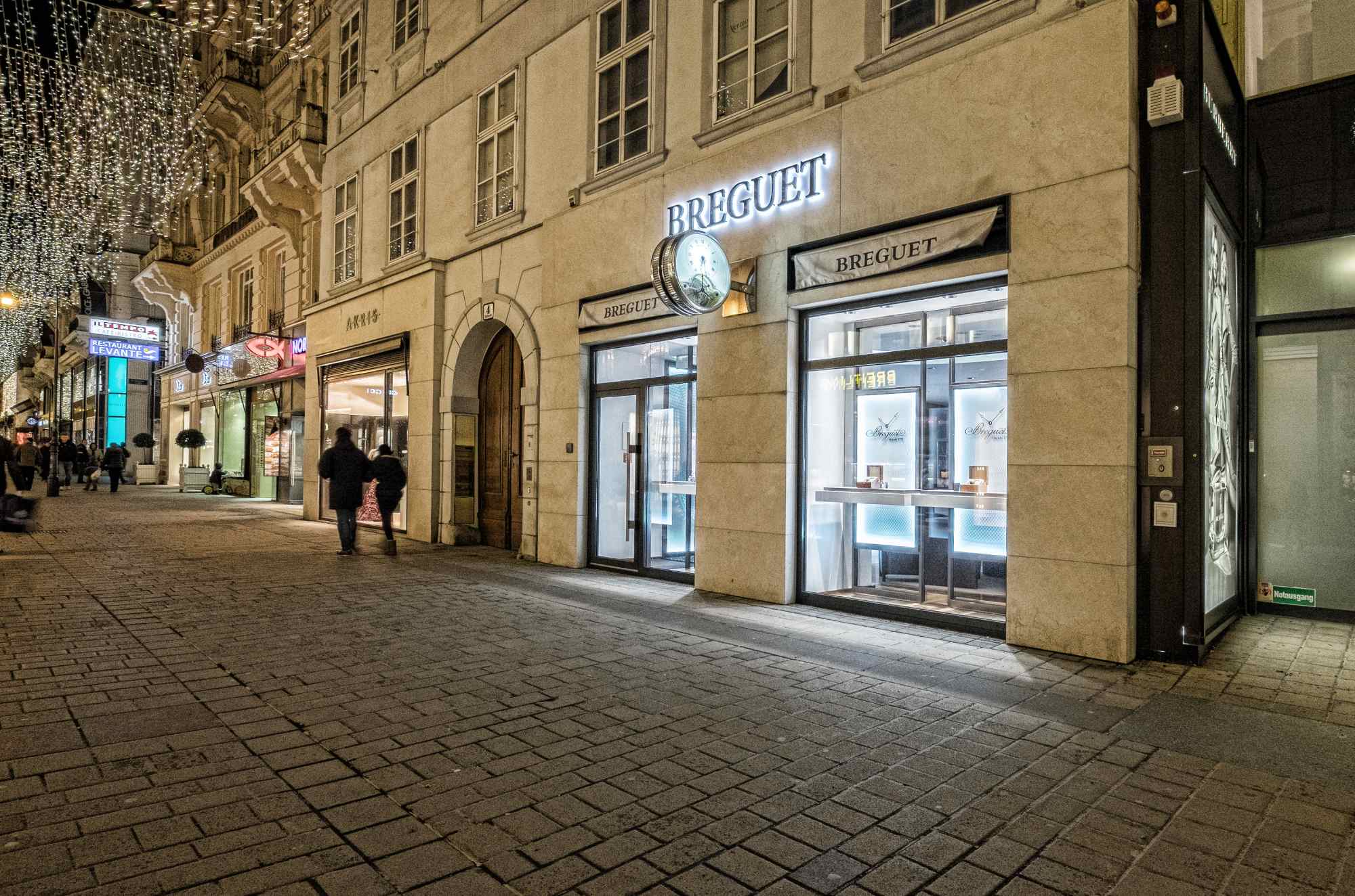 Breguet-Fassade in Fußgängerzone bei Nacht.
