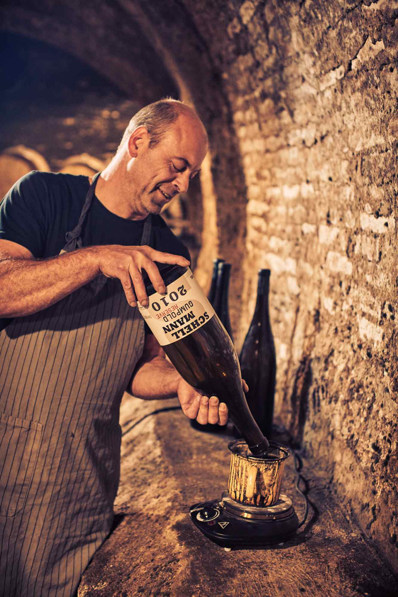 Winzer liest Etikett einer Schellmann-Weinflasche in rustikalem Kellerambiente.