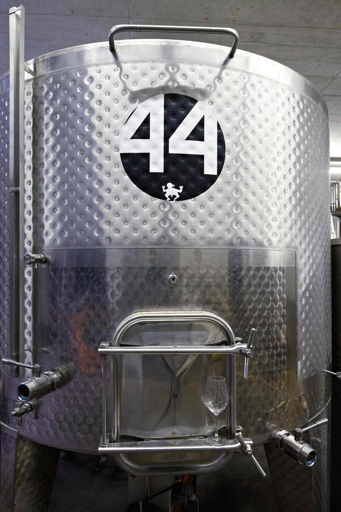Edelstahltank Nummer 44 in moderner Weinkellerei mit angeschlossenem Weinglas zur Weinverkostung.