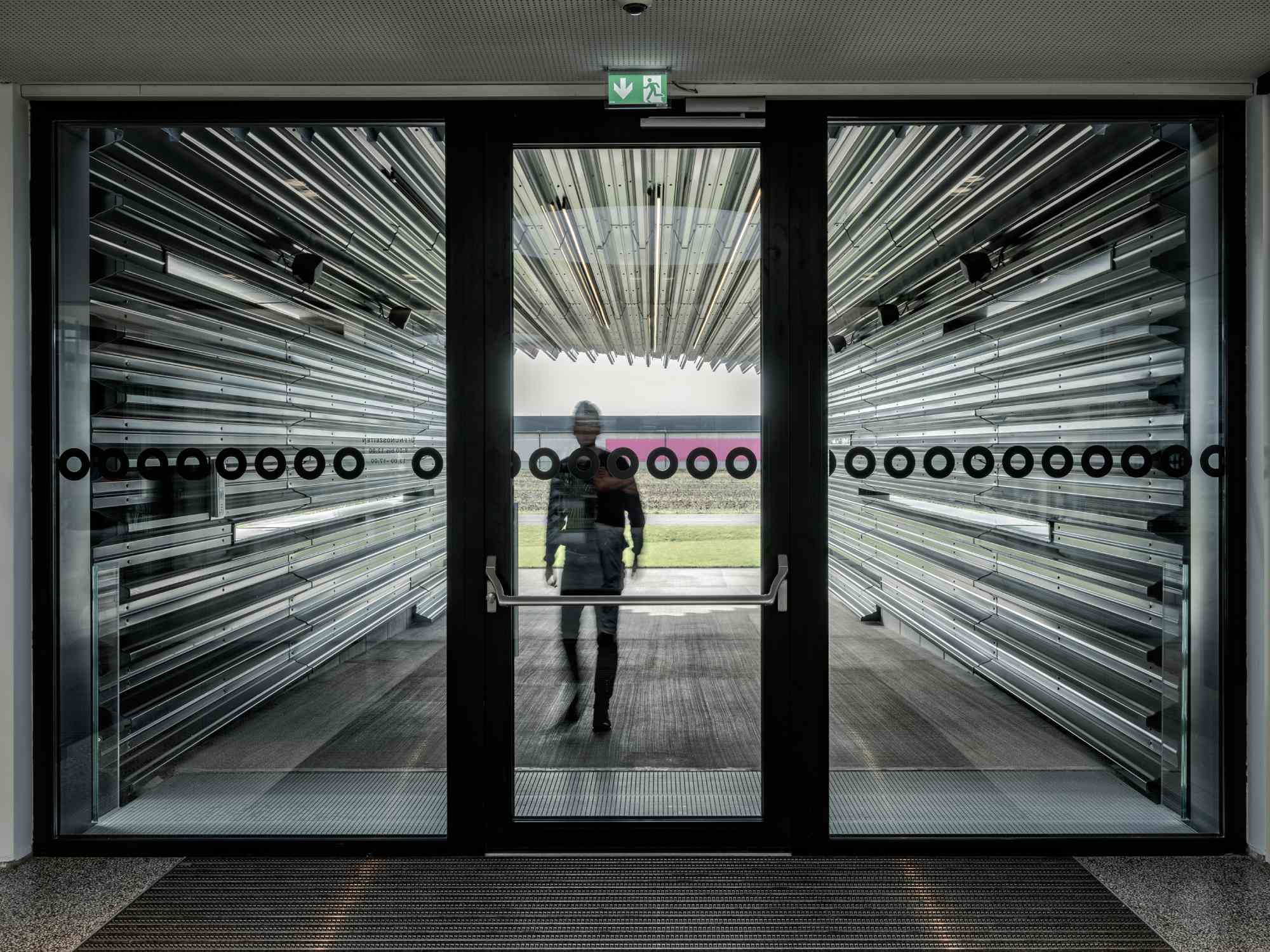 Moderner Eingang mit Glasfront und reflektierenden schwarzen Lamellen.