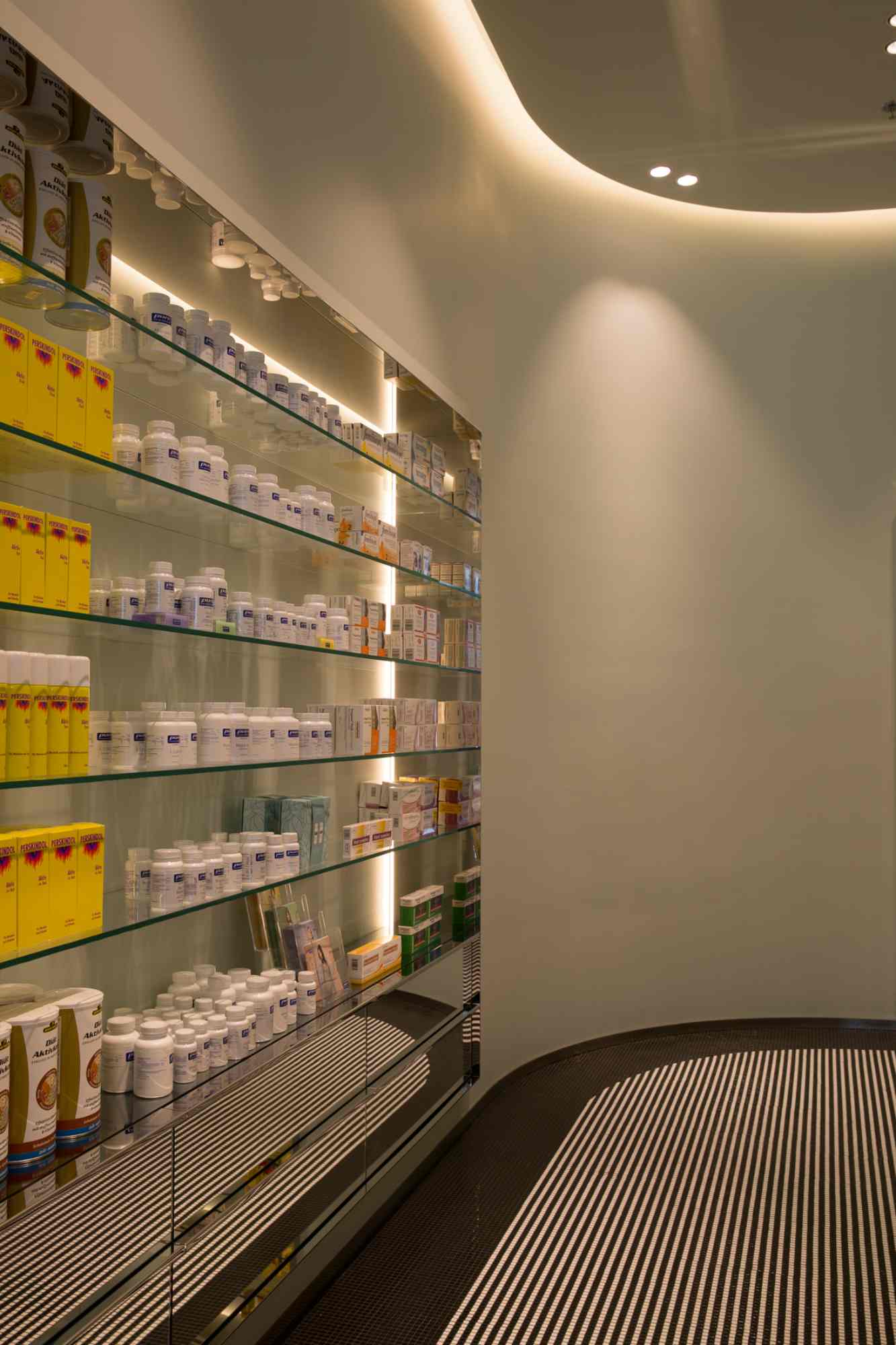 Beleuchtetes Regal mit Arzneimitteln in moderner Apothekenarchitektur.