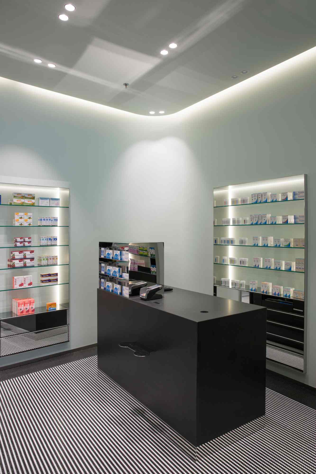 Schwarzer Verkaufstresen vor beleuchteten Apothekenregalen