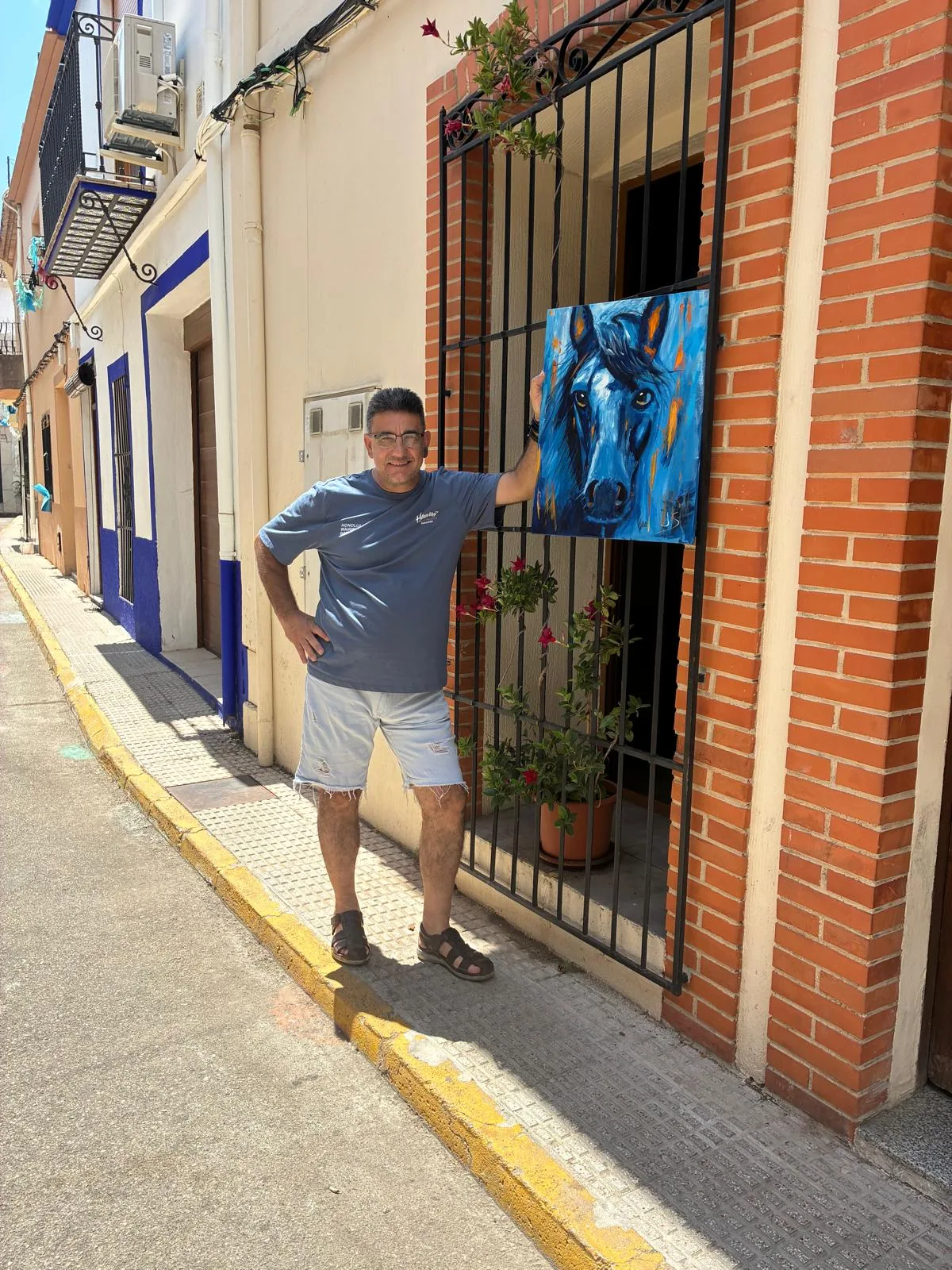 Francisco Javier Seguí García sostiene su cuadro azul de un caballo en una calle de su pueblo