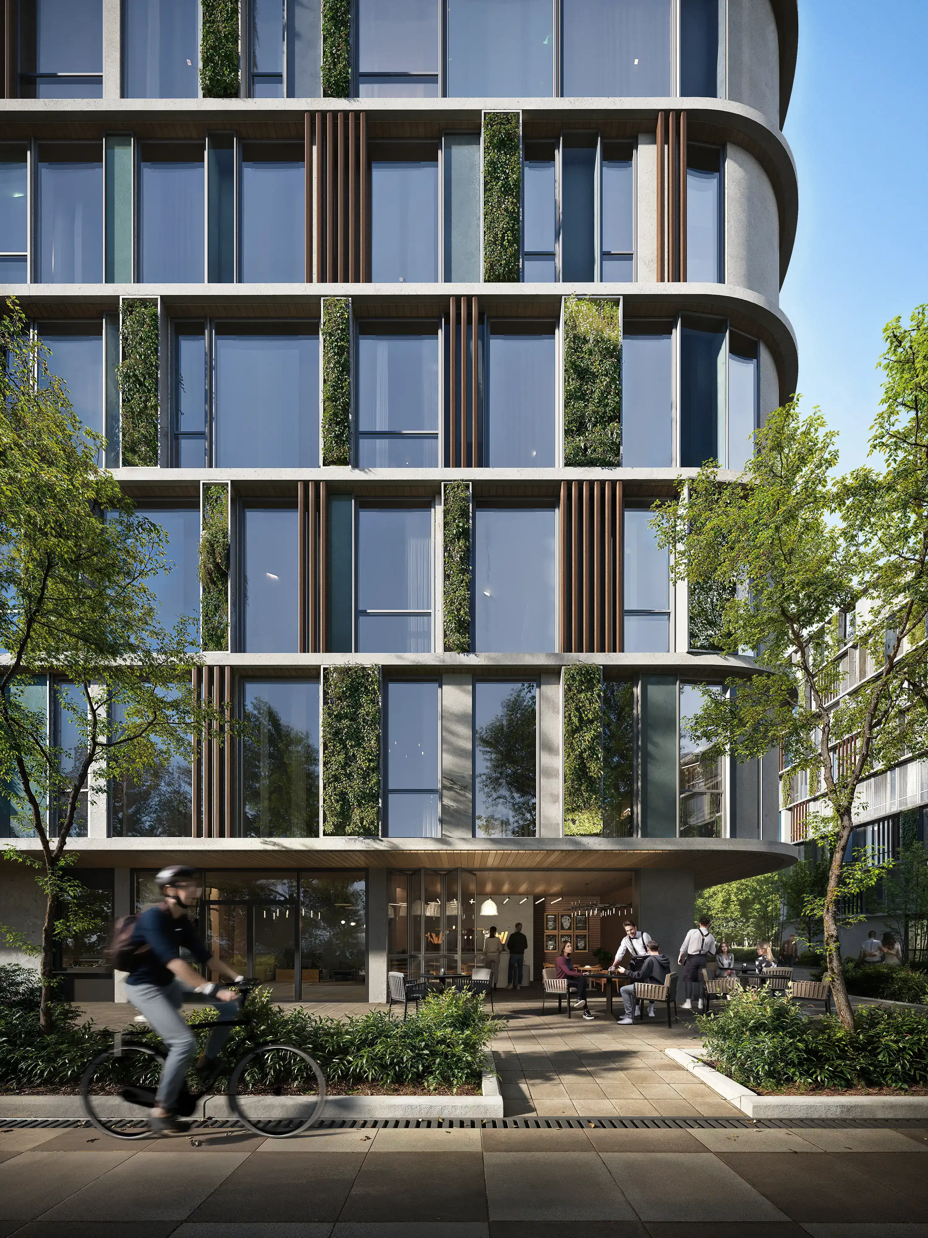 Modern multi-story building with vertical green plant panels on windows, outdoor seating area with people, and a cyclist passing by.