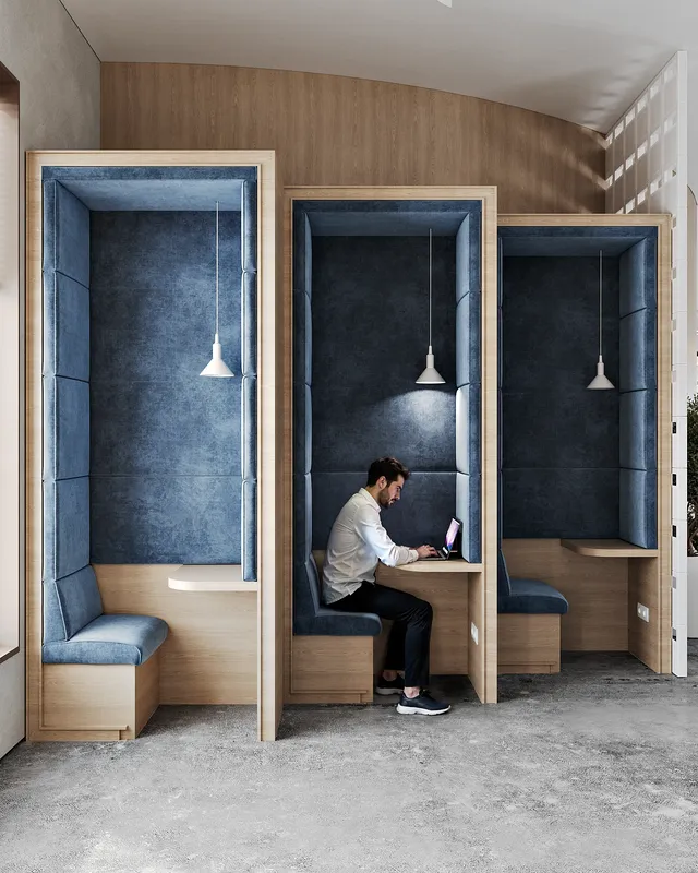 Man working on a laptop inside a private, blue upholstered meeting booth.