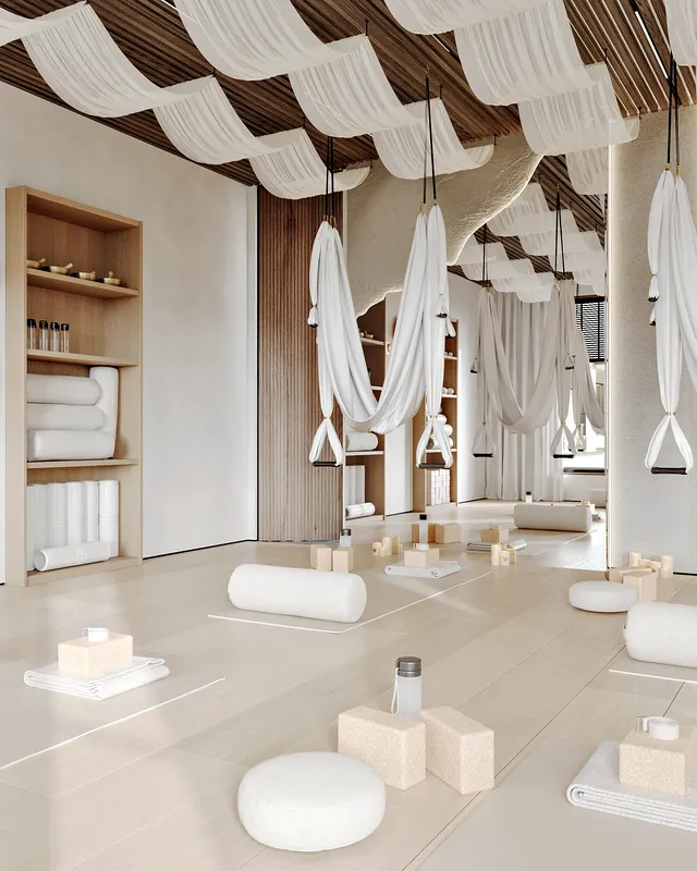 Wide view of a bright yoga studio with mats, hammocks, and an equipment storage shelf.