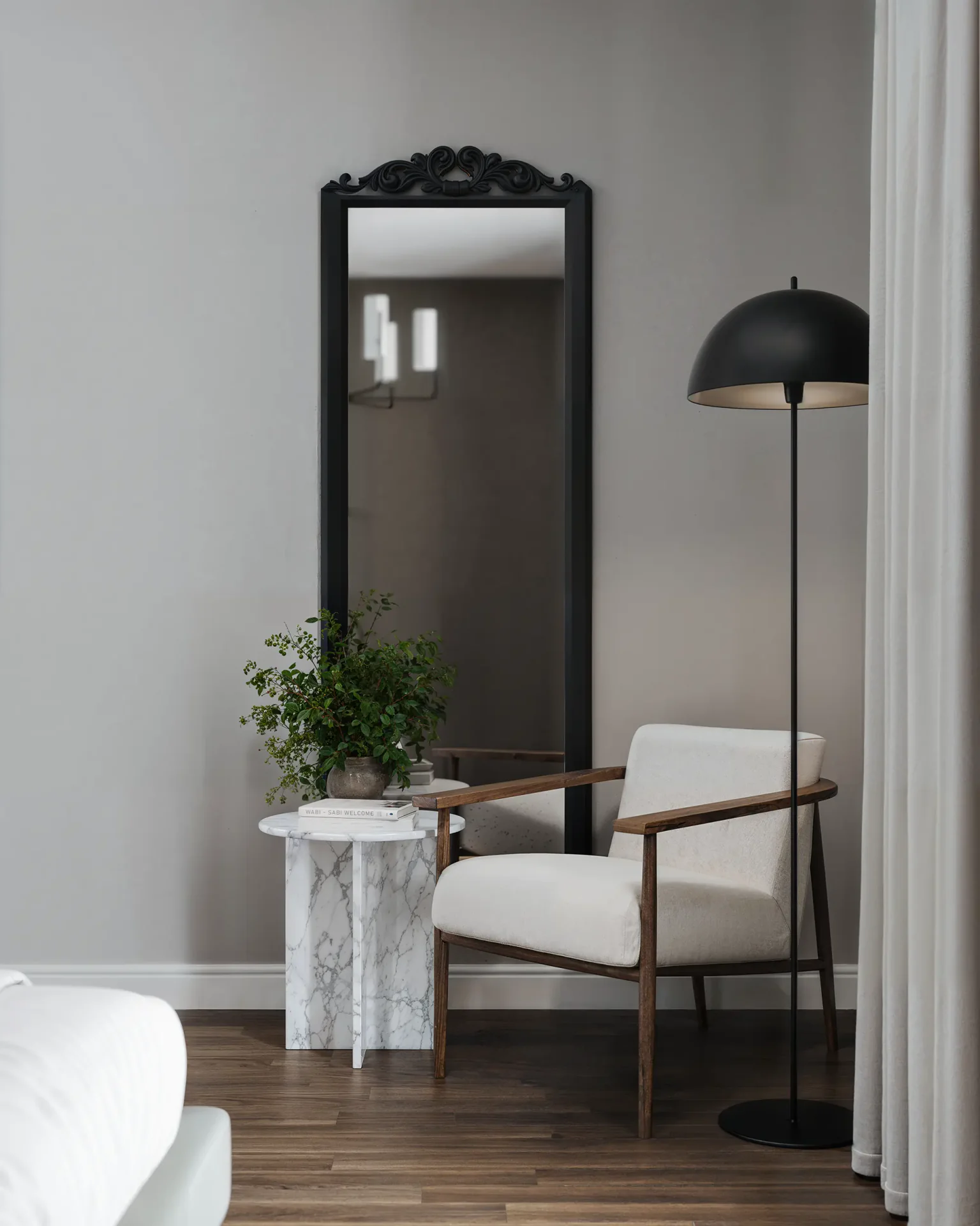 Living room corner with a mirror, floor lamp, and armchair by the window.