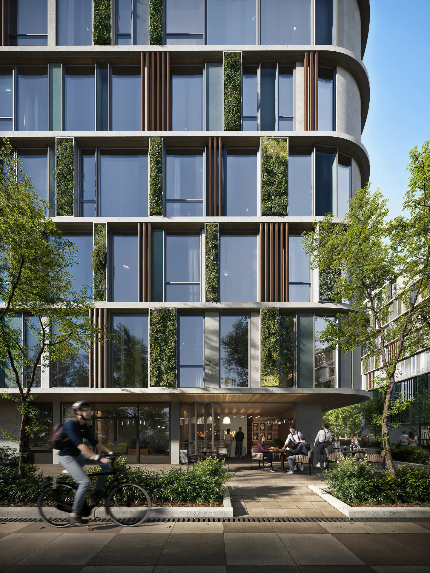 Façade de bâtiment moderne comprenant un café animé au rez-de-chaussée et un cycliste qui passe par là.