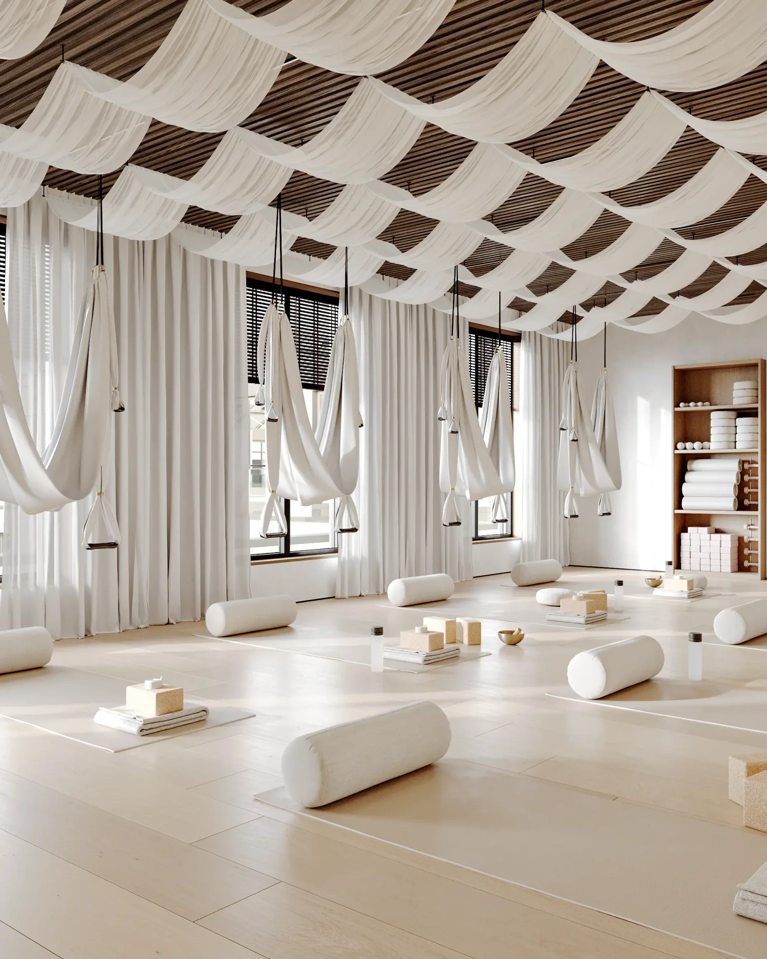 Spacious yoga studio with mats, cushions, and aerial yoga hammocks by the window.