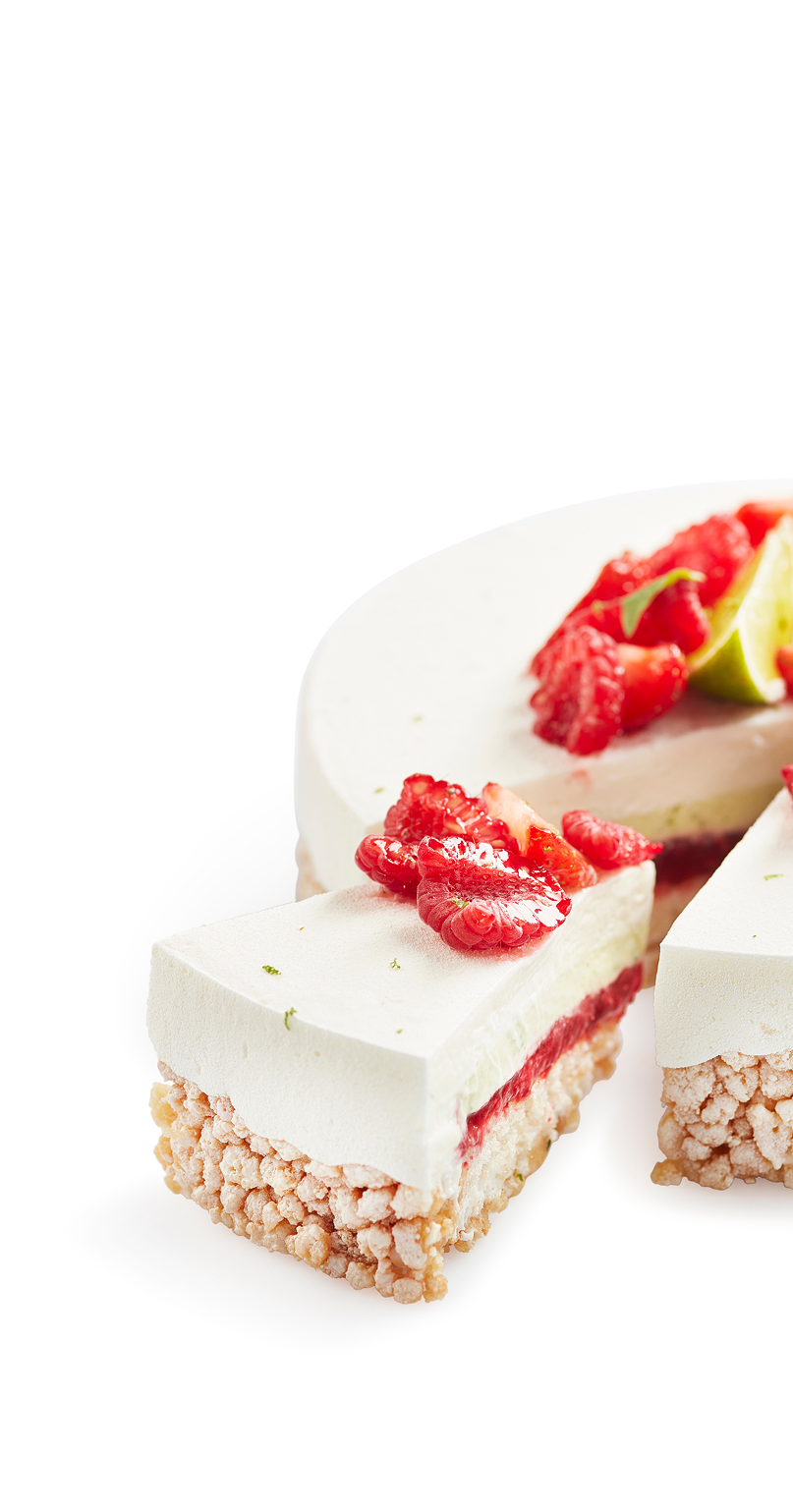 A slice of a layered mousse cake with a crispy puffed rice base, a middle layer of red fruit jelly, and a smooth white mousse topping, garnished with fresh raspberries and lime slices.
