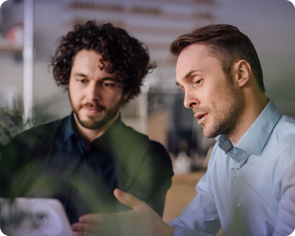 Two men focused on a discussion while looking at a tablet in an office setting.