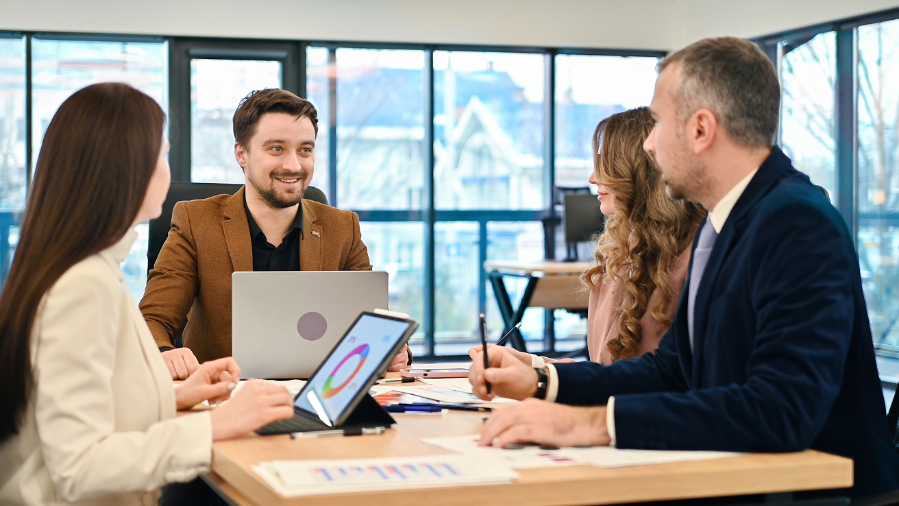 A group of people sitting around a table with laptops.