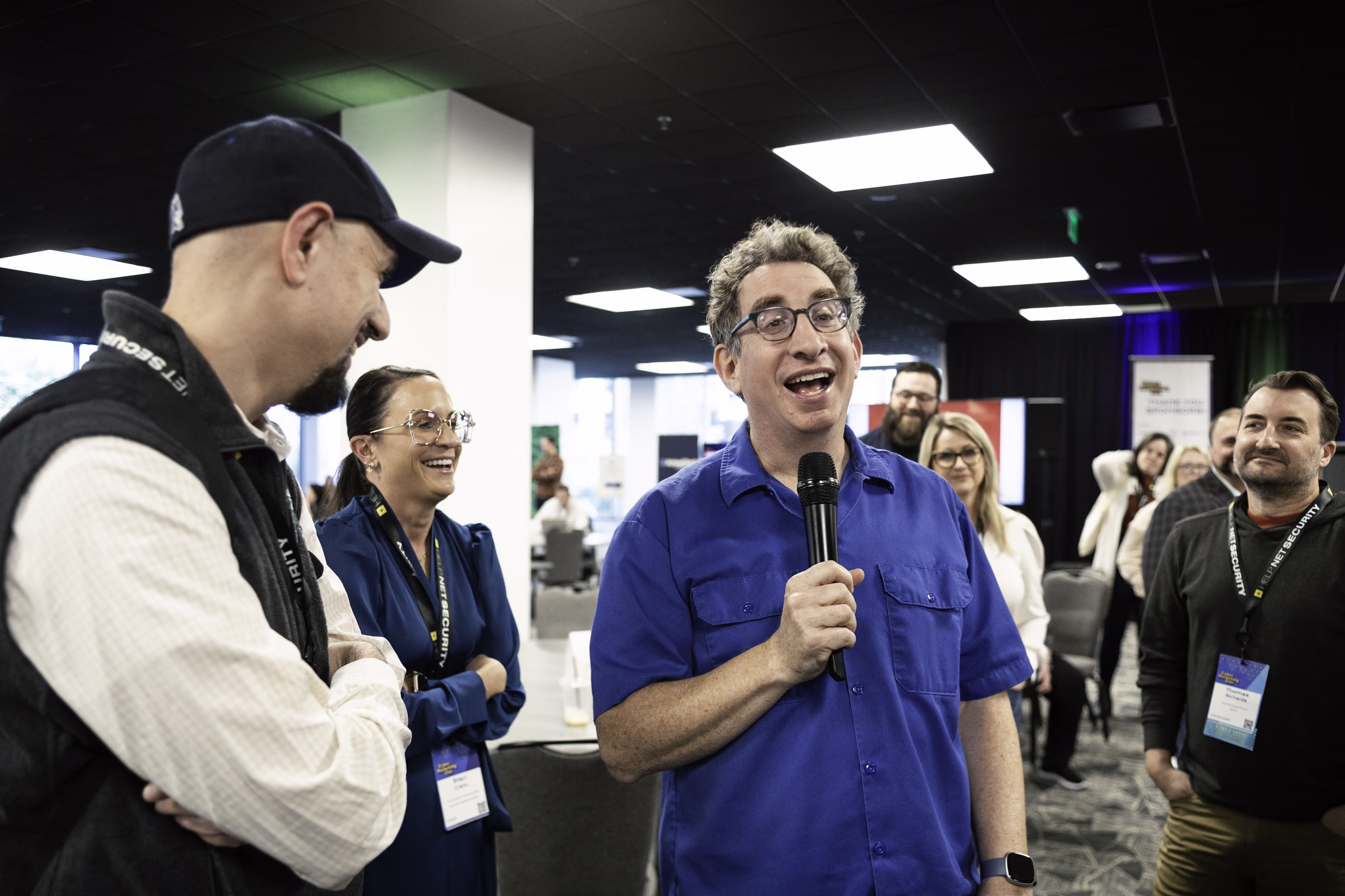 Man speaking into a microphone surrounded by a group of people smiling