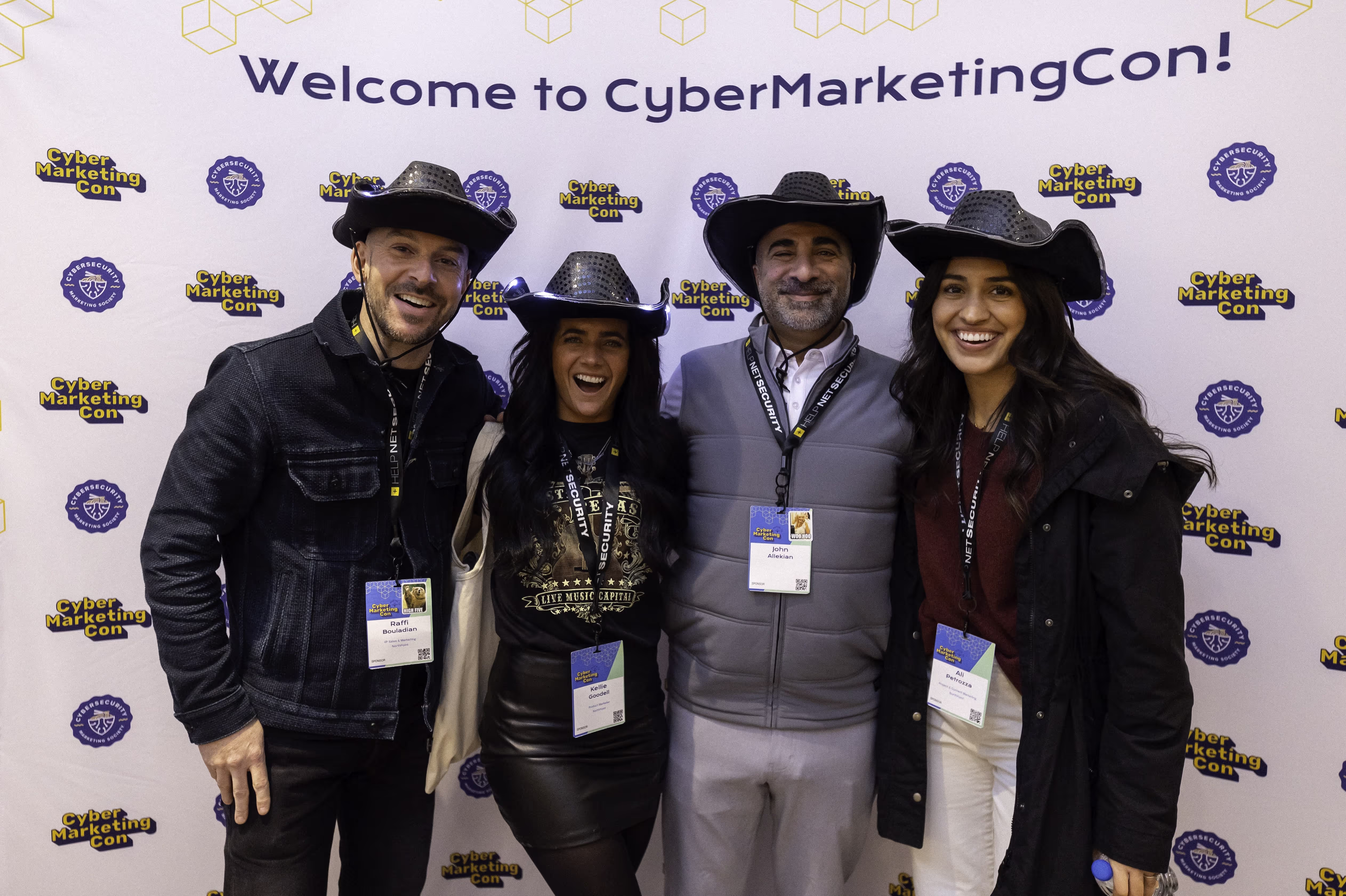 Four people smiling, wearing cowboy hats standing in front of a poster saying welcome to cyber marketing con