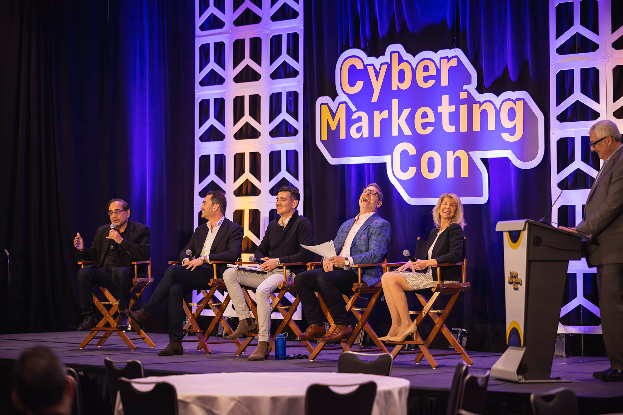 Five people sitting on chairs on a stage behind a poster of cyber marketing con