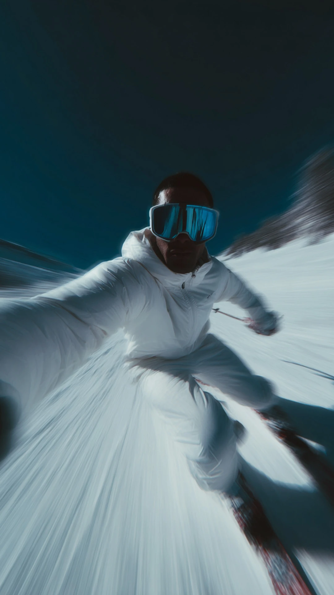 A skier going down the piste taking a selfie. High in motion which indicates the speed. Blue sky, white slopes and subtle sunlight.