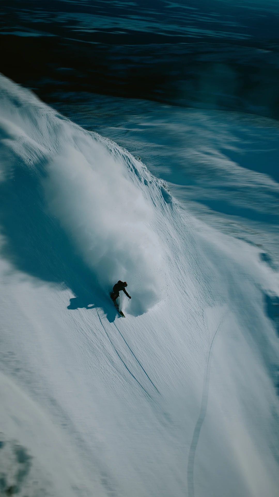 A snowboarder going off piste, leaving a snow cloud. 