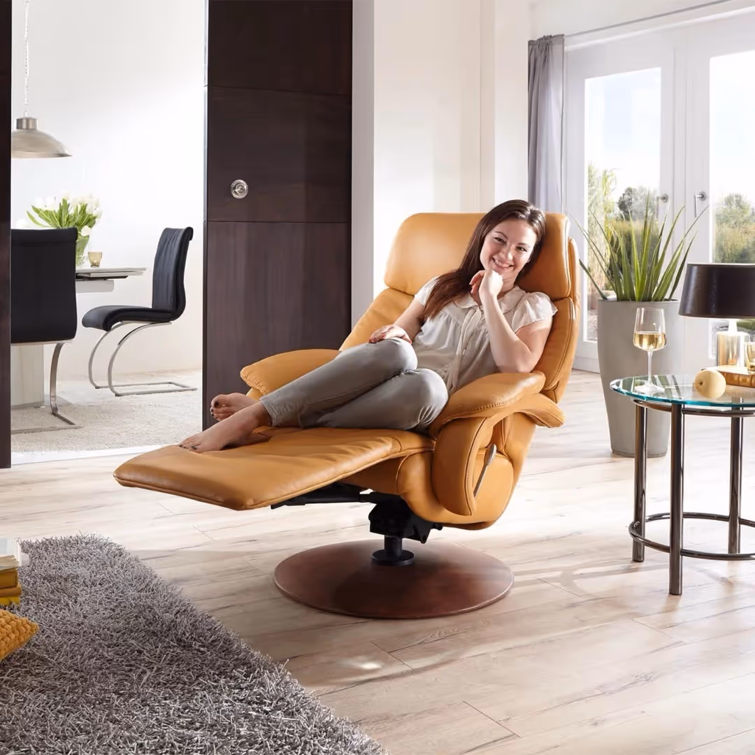 Vrouw ontspannen in een comfortabele gele leunstoel met voetensteun in een lichte woonkamer.