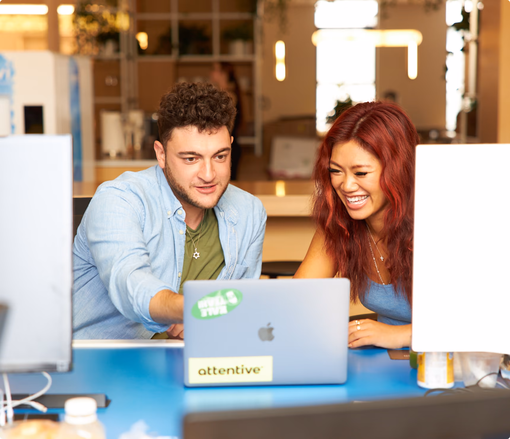 Two smiling colleagues looking at a laptop screen together in a bright office space.