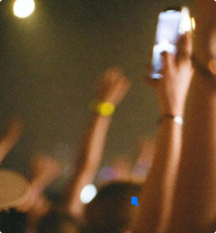 Blurry crowd at event with raised hands and one person holding up a smartphone.