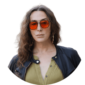Person with curly hair wearing orange-tinted sunglasses and denim jacket