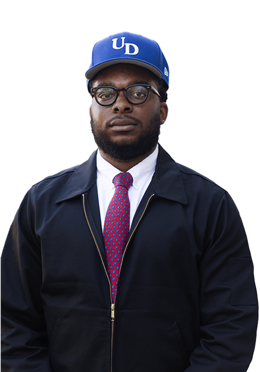 Person wearing UD cap, glasses, navy jacket, and red patterned tie