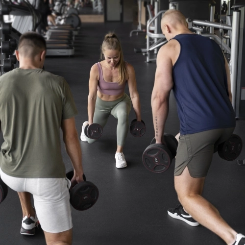 Three individuals lifting dumbbells in a CrossFit gym in Waveland, MS, focused on their workout routine.