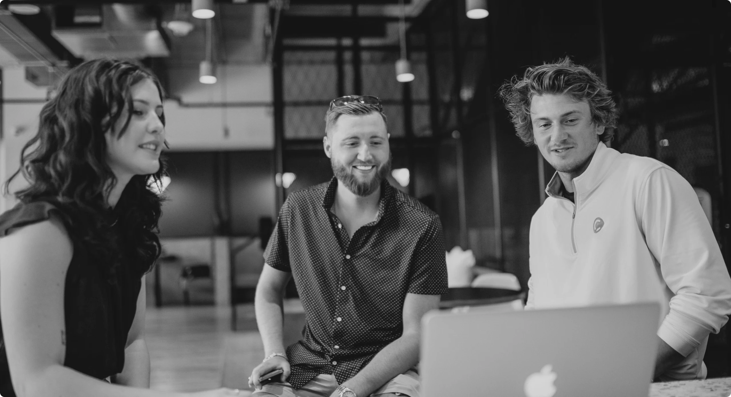 Three team members collaborating around a laptop in a modern office environment.