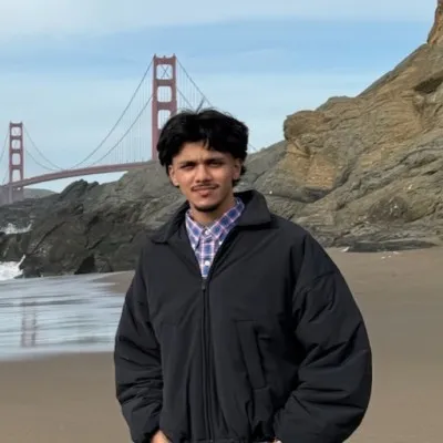 Man with a beard wearing a tan baseball cap and black shirt against a light purple background.