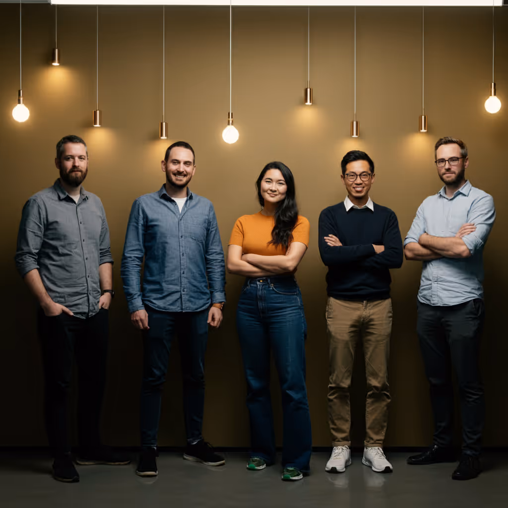 Group of five diverse young professionals standing with arms crossed under hanging light bulbs.