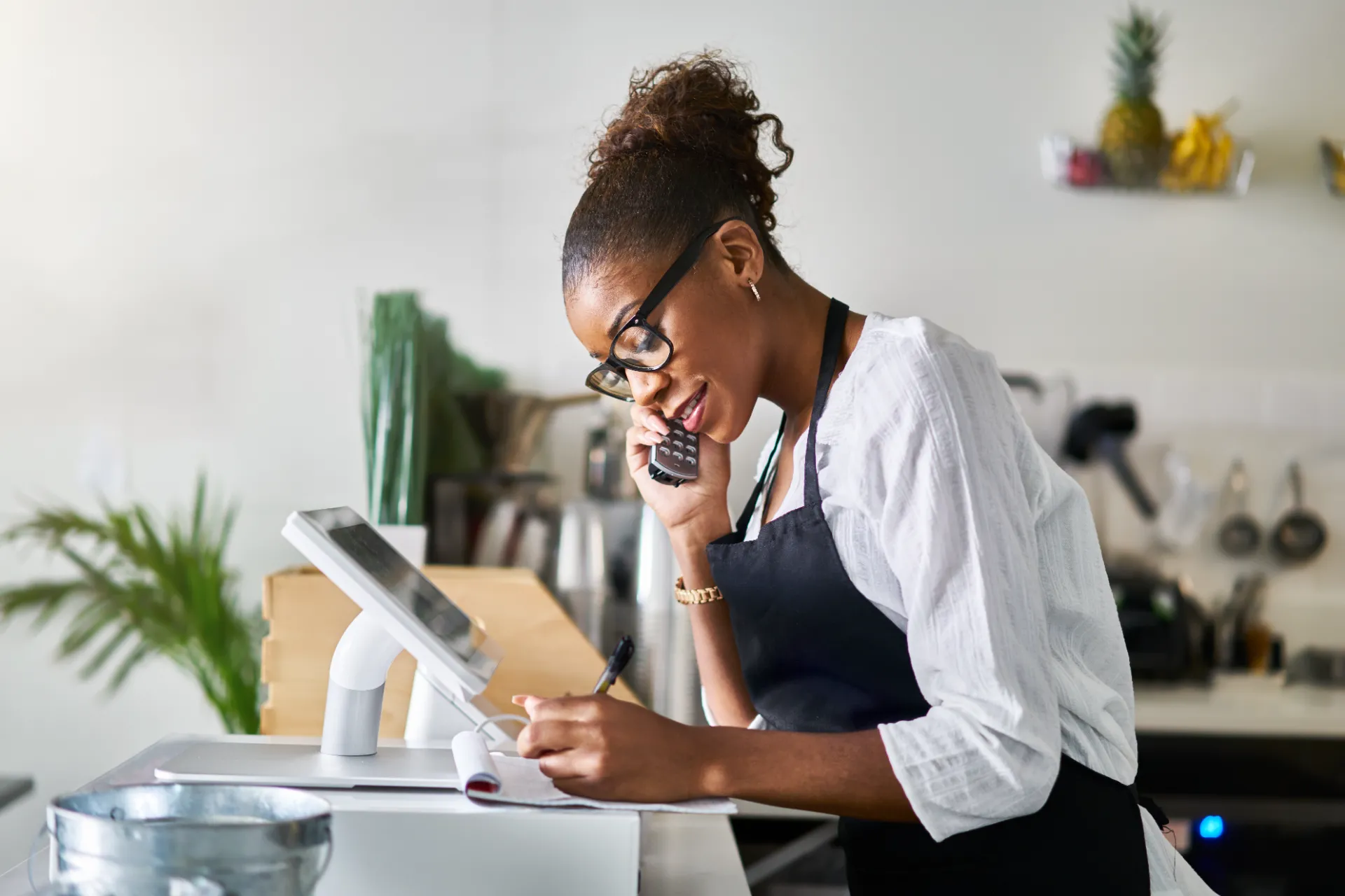 Friendly business owner taking order on phone at restaurant and writing on notepad