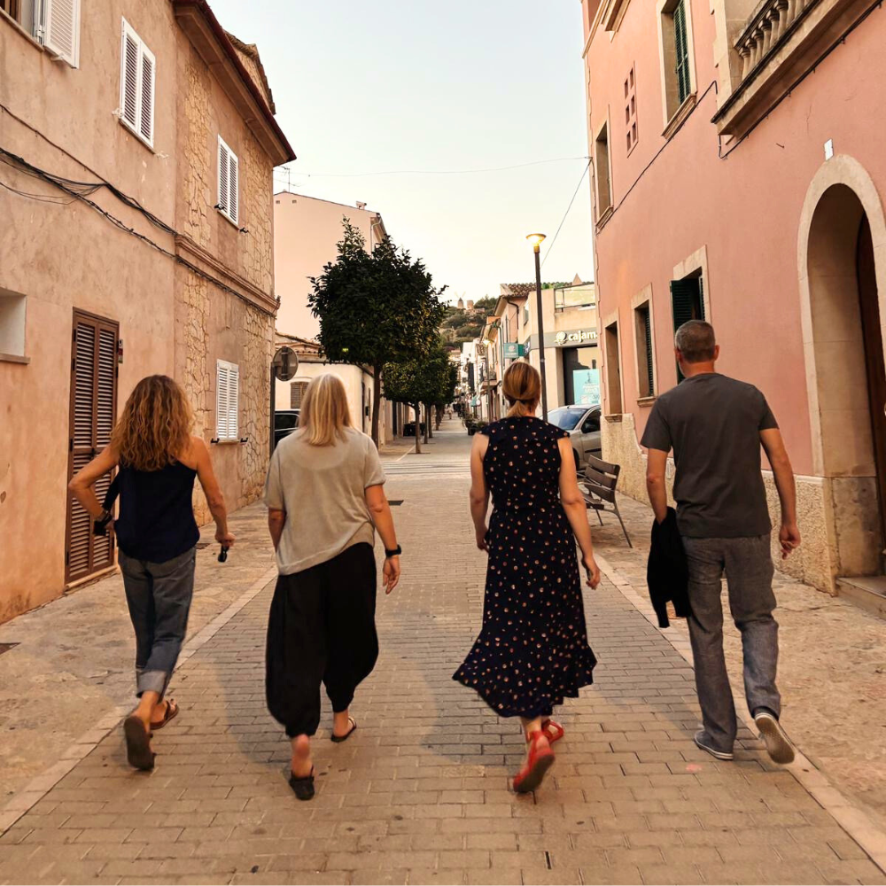 Mallorca retreat guests walking down a narrow cobblestone street lined with peach-colored buildings and trees.