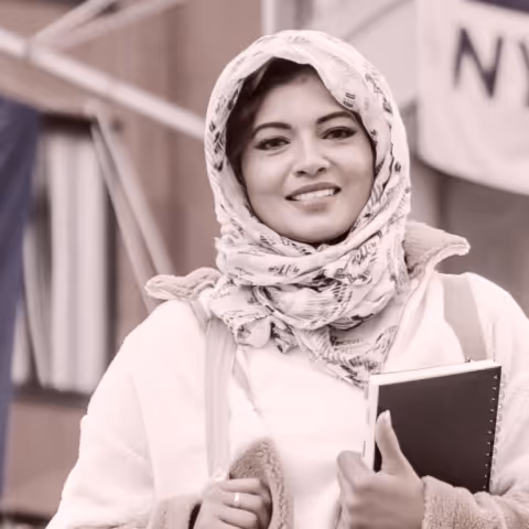 Woman with a head scarf holding a notebook and smiling
