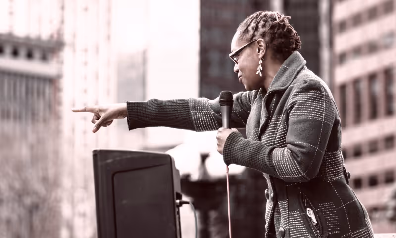 A black woman holding a microphone speaking to a crowd from a stage