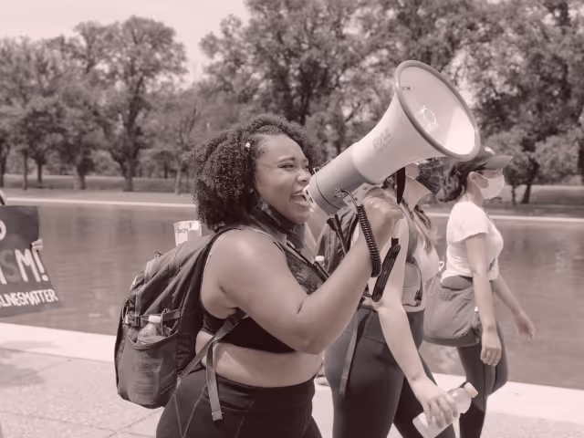 A young black woman marching and speaking into a megaphone