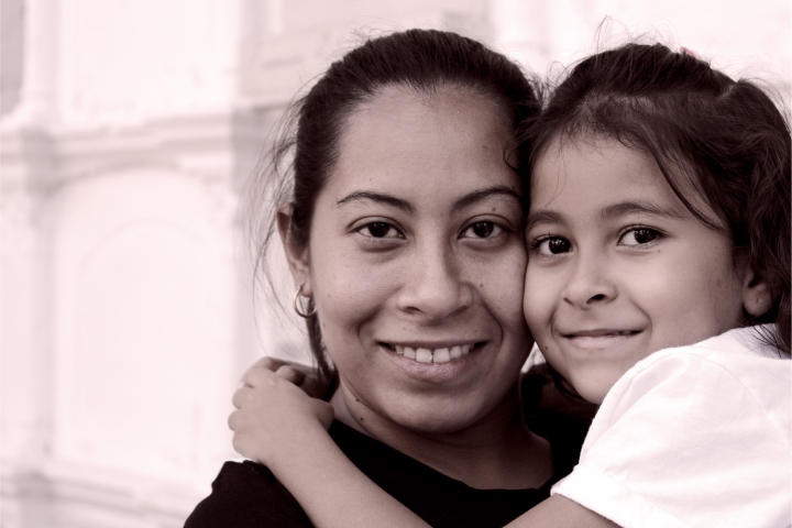 A Latinx woman holding her young daughter and smiling