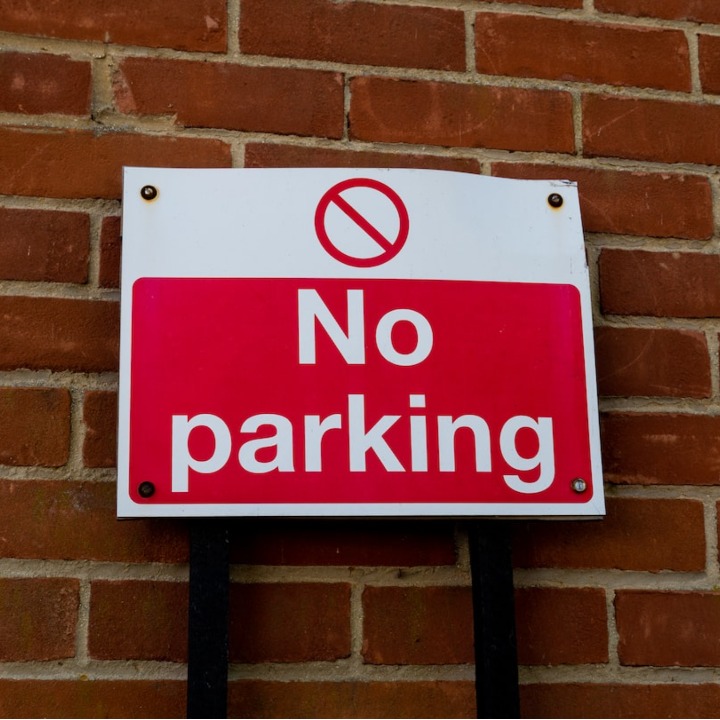 Red and white no parking sign mounted on brick wall