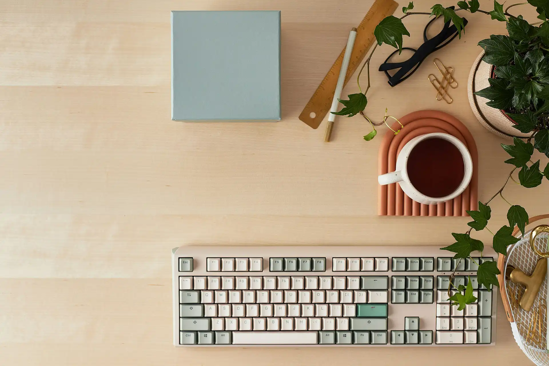 Minimalist workspace with keyboard, cup of tea, and plants on a wooden desk