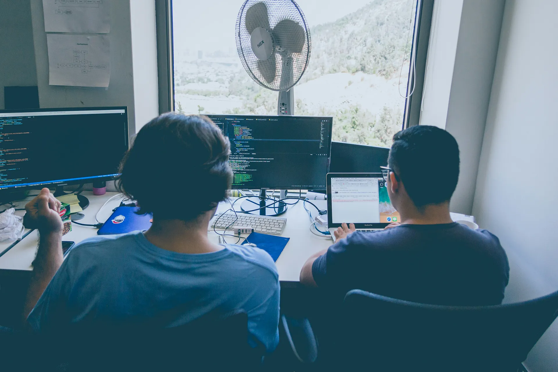 Two software developers collaborating at a workstation with multiple monitors displaying code